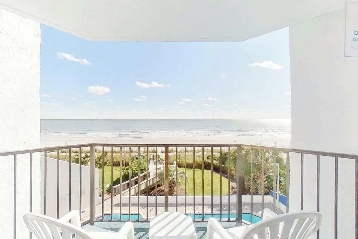 A balcony with a view of the ocean, a pool, and a lawn.