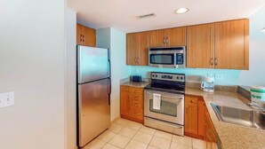 A kitchen with wooden cabinets, stainless steel appliances, a microwave, oven, and a sink. - Sandy Beach Resort 504 (Myrtle Beach)