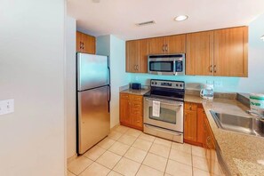 A kitchen with wooden cabinets, stainless steel appliances, a microwave, oven, and a sink. - Sandy Beach Resort 504 (Myrtle Beach)