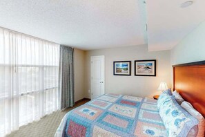 A hotel room with a bed, a window with curtains, a door, and two framed pictures on the wall. - Sandy Beach Resort 504 (Myrtle Beach)
