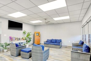 Ein Zimmer mit Rattanmöbeln, einem Deckenventilator, einem Flachbildfernseher und einem Automaten.