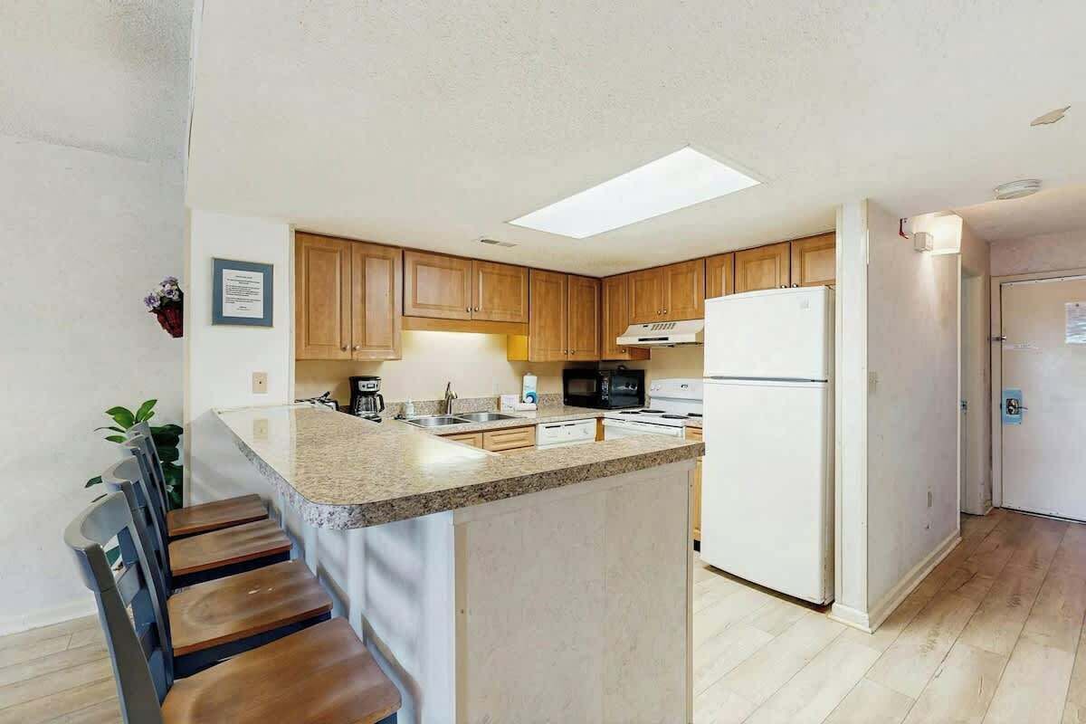 Una cocina con armarios de madera, un refrigerador blanco, un microondas y una encimera de granito.