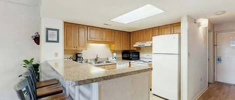 Una cocina con armarios de madera, un refrigerador blanco, un microondas y una encimera de granito.
