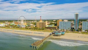 A coastal cityscape with a pier, a large Ferris wheel, and modern buildings. - Sea Mark Tower Unit 205 (Myrtle Beach)