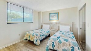 A bedroom with two beds, a window with blinds, a bedside table with a lamp, and a framed picture on the wall. - Sea Mark Tower Unit 205 (Myrtle Beach)