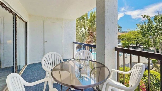A balcony with a glass table and white chairs, overlooking a residential area with palm trees and houses. - Sea Mark Tower Unit 205 (Myrtle Beach)
