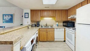 A kitchen with wooden cabinets, a washing machine, a microwave, and a stove. - Sea Mark Tower Unit 205 (Myrtle Beach)