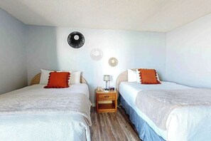 Quarto com duas camas, uma mesa de cabeceira e luminária fixada na parede.
