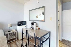 A compact room with a bed, a small bedside table with a lamp, a microwave, a coffee maker, and a chair. - Ocean Park Resort 0922/0924 Combo (Myrtle Beach)