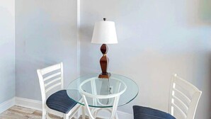 A small round glass table with two white chairs, a white lamp, and a plain wall. - Ocean Park Resort 0922/0924 Combo (Myrtle Beach)