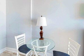A small round glass table with two white chairs, a white lamp, and a plain wall. - Ocean Park Resort 0922/0924 Combo (Myrtle Beach)