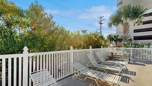 Ein Balkon mit weißen Geländern, mehreren Liegestühlen und einer Palme.