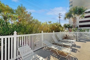 Ein Balkon mit weißen Geländern, mehreren Liegestühlen und einer Palme.