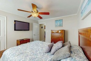 Ein Schlafzimmer mit Bett, Deckenventilator, Fernseher, Kommode und einem Gemälde an der Wand.