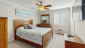 Ein Schlafzimmer mit einem Bett, einem Deckenventilator, einem Schminktisch, einem Spiegel und einem Fernseher.