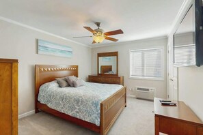 Ein Schlafzimmer mit einem Bett, einem Deckenventilator, einem Schminktisch, einem Spiegel und einem Fernseher.