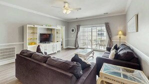 Un salon avec un canapé, un téléviseur et une table basse en verre.