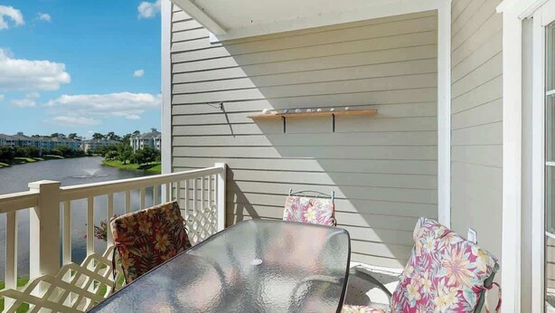 Un balcon avec une table en verre et deux chaises, une balustrade blanche et une vue sur une route et la verdure.
