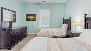 Une chambre à coucher comprenant un lit, une commode, une table de chevet, une lampe, une fenêtre avec des stores et un ventilateur de plafond.