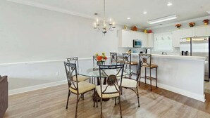 Une cuisine moderne avec des meubles blancs, un réfrigérateur en acier inoxydable et un coin repas comprenant une table en verre et des chaises en métal.