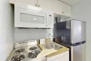 A compact kitchen with a microwave, stove, sink, and refrigerator. - Pelicans Flight at Sandcastle South (Myrtle Beach)