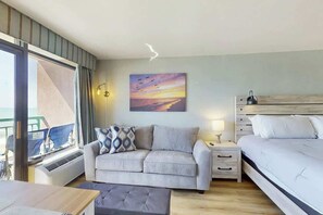 A bedroom with a bed, a sofa, a bedside table, and a painting on the wall. - Pelicans Flight at Sandcastle South (Myrtle Beach)