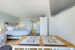 A hotel room with a bed, bedside table, and a desk with placemats. - Pelicans Flight at Sandcastle South (Myrtle Beach)