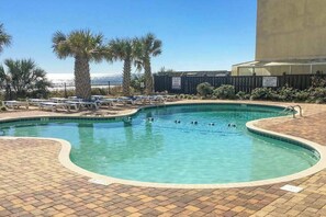 Ein Pool mit Liegestühlen und Palmen, umgeben von einer Ziegelterrasse.