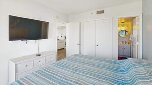 A bedroom with a bed, a television mounted on the wall, a wardrobe, and a bathroom visible through an open door. - Palace Resort Unit 1508 (Myrtle Beach)