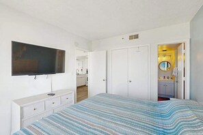 Ein Schlafzimmer mit einem Bett, einem an der Wand befestigten Fernseher, einem Kleiderschrank und einem durchgegangenen Tür erkennbaren Badezimmer.