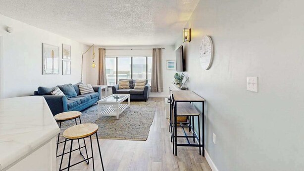 A modern living room with a sofa, coffee table, and a dining area with a table and chairs. - Palace Resort Unit 1508 (Myrtle Beach)