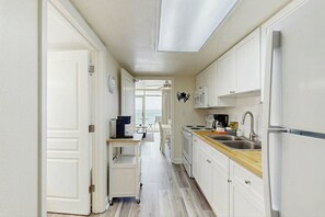 A narrow kitchen with white cabinets, a wooden countertop, and a refrigerator. - Bay Watch Resort 0903 (North Myrtle Beach)