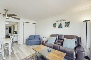 A living room with a brown leather sofa, a blue armchair, a wooden coffee table, and a ceiling fan. - Bay Watch Resort 0903 (North Myrtle Beach)