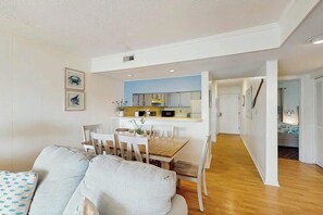 A modern living room with a dining area, a kitchen in the background, and a hallway leading to another room. - Afterdeck Unit 203 Condo (Murrells Inlet)