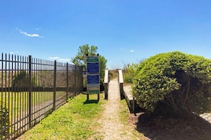 A pathway leading to a gated area with a signboard, surrounded by a fence and greenery. - Sandtrap at the Verandas (North Myrtle Beach)
