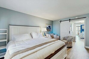 A bedroom with a large bed, a bedside table, a chair, and a door leading to another room. - Sandtrap at the Verandas (North Myrtle Beach)