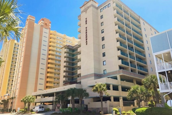 A multi-story hotel with a central courtyard, palm trees, and a parking area. - Sandtrap at the Verandas (North Myrtle Beach)