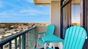 Un balcón con dos sillas y una mesa, con vista a una zona residencial que incluye casas y una calle.