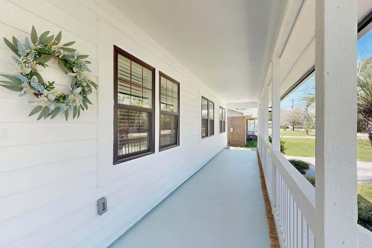 A covered porch with white siding and large windows, leading to a brick structure.