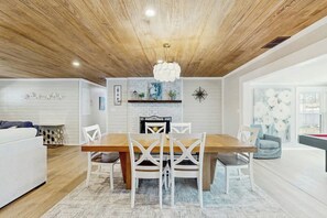 A modern living room with a wooden ceiling, a dining table with chairs, a fireplace, and a pool table. - Coastal Retreat on Bay Street (North Myrtle Beach)