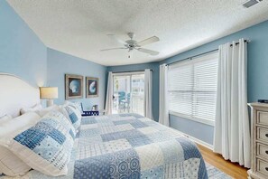Ein Schlafzimmer mit Bett, Deckenventilator, Fenster mit Jalousien und Blick ins Freie.