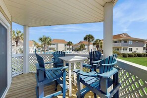 A covered outdoor seating area with blue chairs and a white table, overlooking a residential neighborhood with houses and palm trees. - Shorehaven Unit W-2 Condo (North Myrtle Beach)