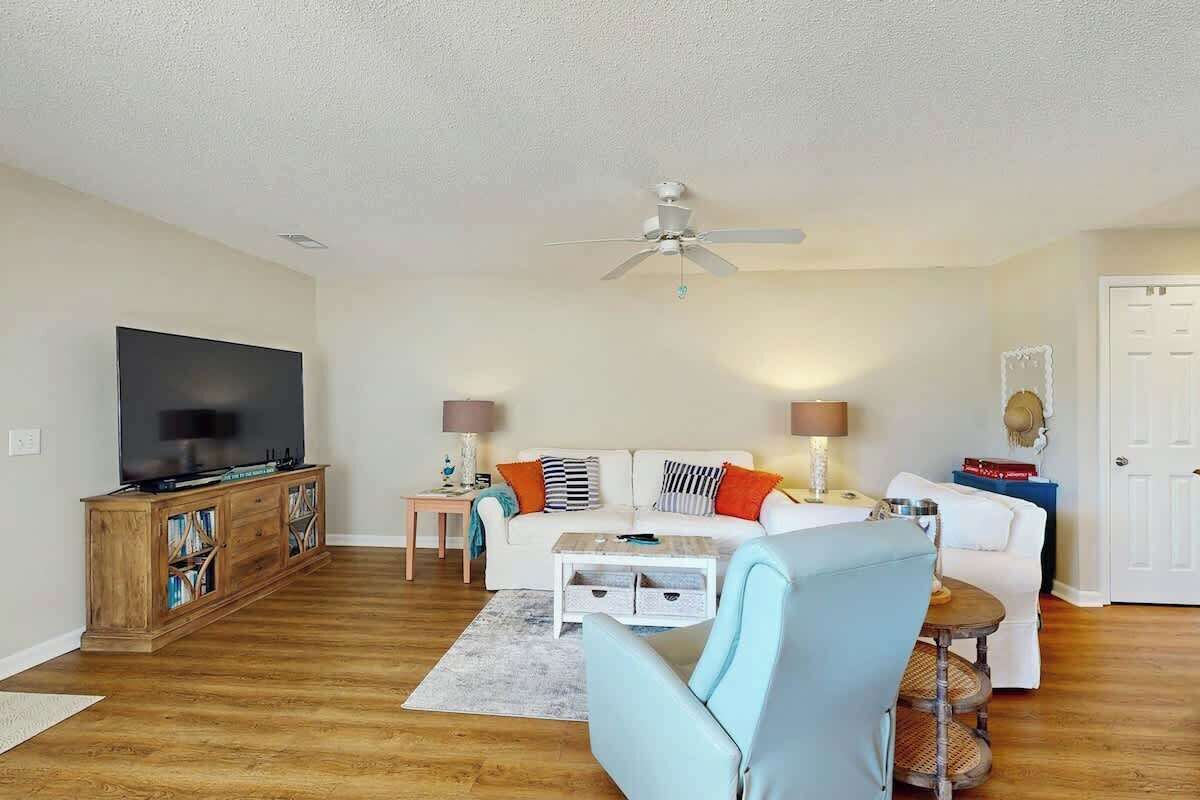 A living room with a flat-screen TV, a white sofa, a blue armchair, a coffee table, and a ceiling fan.