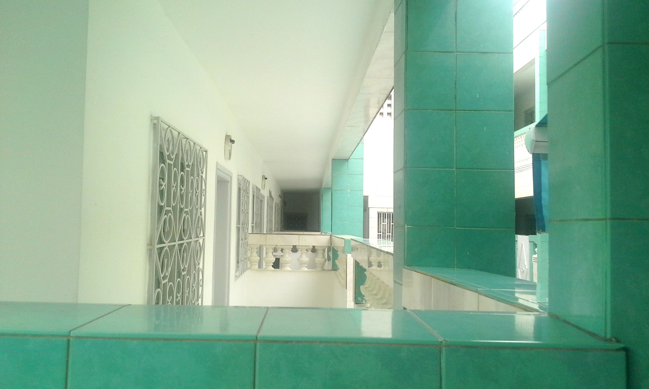 A corridor with a tiled floor, a staircase, and a railing.
