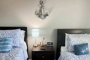 A hotel room with two beds, each with patterned bedding, a nightstand with a lamp, an anchor decoration, and a clock. - River Oaks Unit 25A Condo (Myrtle Beach)