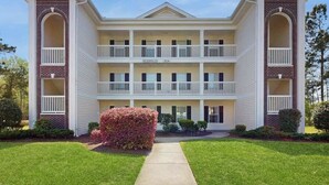 A multi-story building with a central entrance, balconies on each floor, and a brick facade. - River Oaks Unit 25A Condo (Myrtle Beach)
