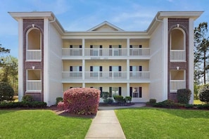 A multi-story building with a central entrance, balconies on each floor, and a brick facade. - River Oaks Unit 25A Condo (Myrtle Beach)