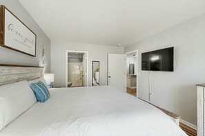 A hotel room with a large bed, a television mounted on the wall, and a door leading to a bathroom. - River Oaks Unit 25A Condo (Myrtle Beach)