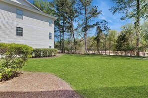 A two-story house with a well-maintained lawn and a stone wall in the background. - River Oaks Unit 25A Condo (Myrtle Beach)