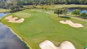 Um campo de golfe com bunkers de areia, lago e árvores.